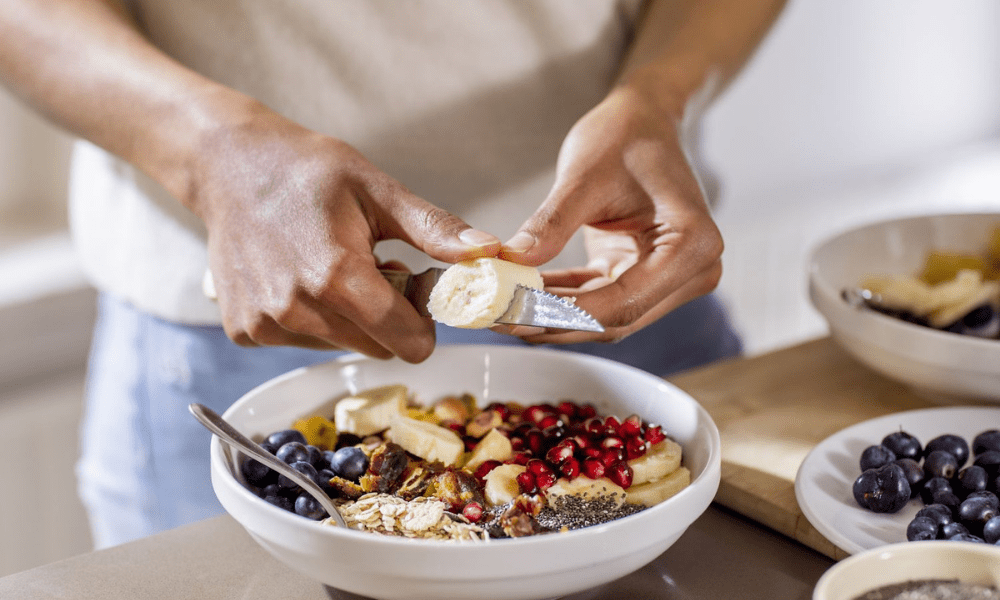 A man cutting banana in a bowl full of healthy food items. - Health Diet