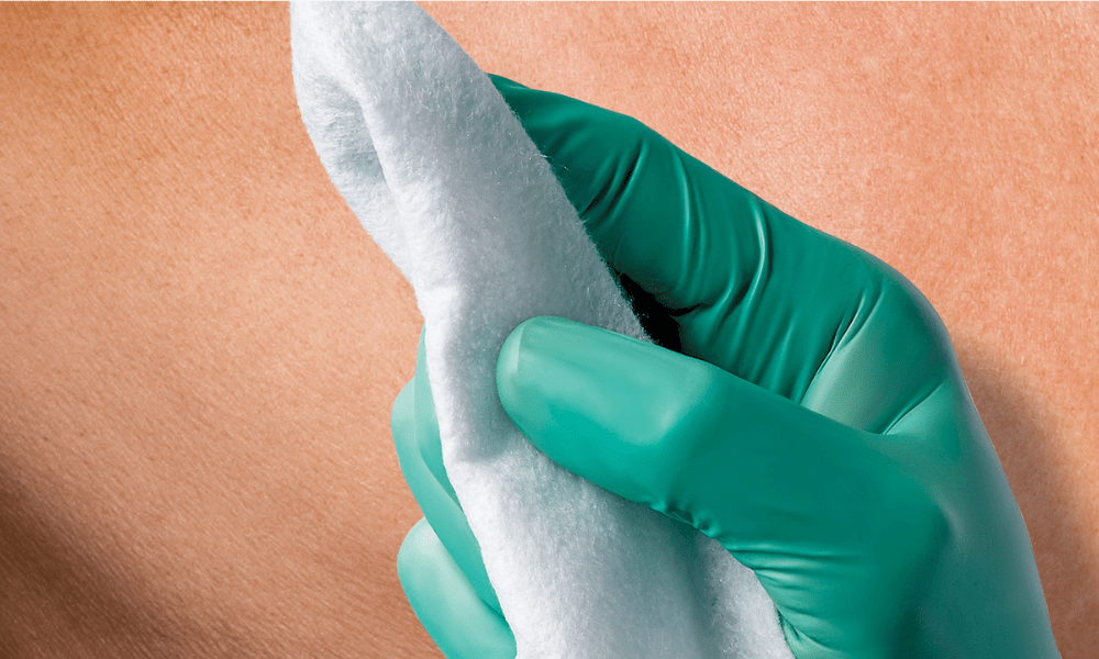 Perineal care: Gloved hand holding a cotton pad against skin, representing perineal care and hygiene.